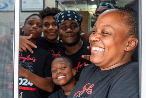 Jaybee’s Tenders co-founder Erika Harrington laughs while posing for a portrait as her sons and manager Qú Jones, third from left, pose behind her at Jaybee's Tenders in Decatur, GA on Thursday, July 25, 2024. (Seeger Gray / AJC)