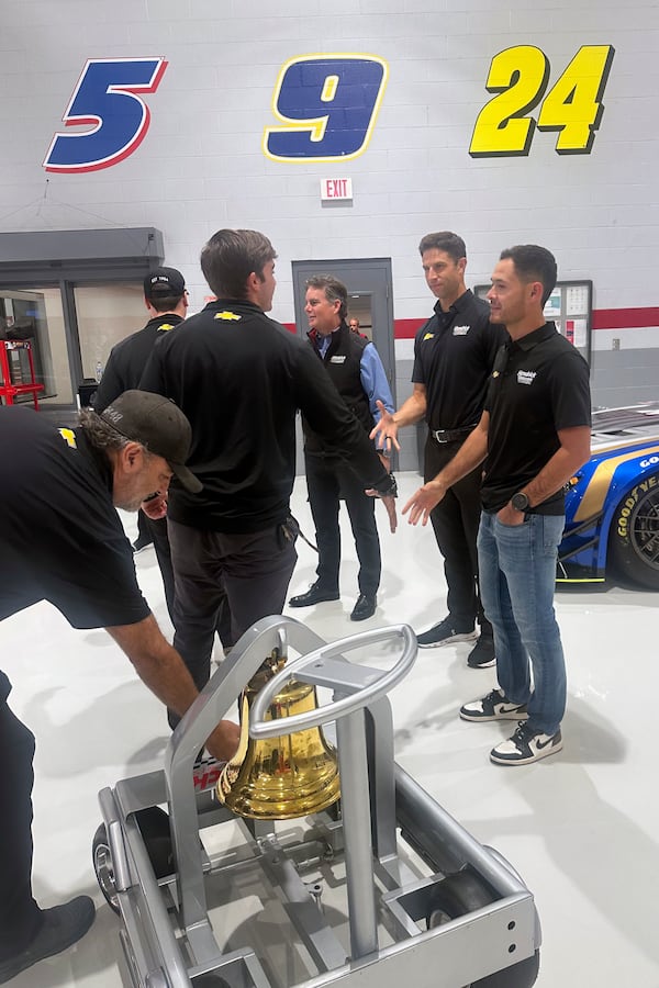 Hendrick Motorsports vice chairman Jeff Gordon, center rear, crew chief Cliff Daniels, second from right, and NASCAR driver Kyle Larson shake hands with Hendrick Motorsports teammates during the victory bell ringing ceremony for Larson’s win at Bristol Motor Speedway, Oct. 9, 2024, at Hendrick Motorsports in Charlotte, N.C. (AP Photo/Jenna Fryer)