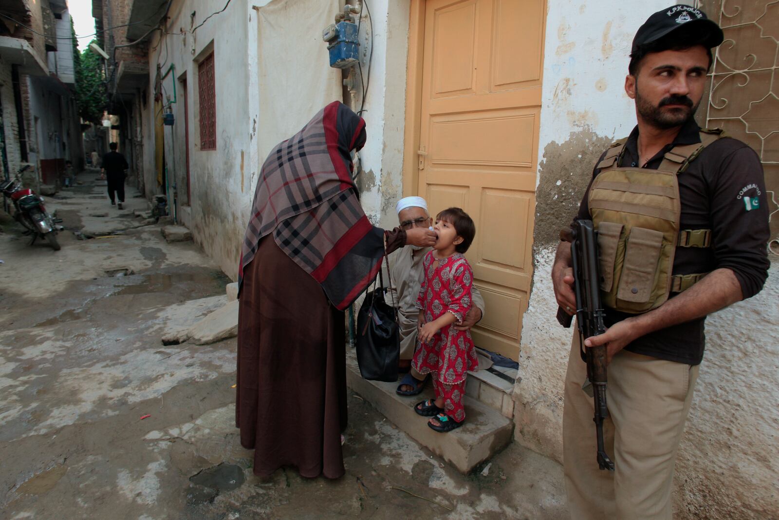 A police officer stands guard as a health worker, center, administers a polio vaccine to a child in a neighbourhood of Peshawar, Pakistan, Monday, Oct. 28, 2024. (AP Photo/Mohammad Sajjad)