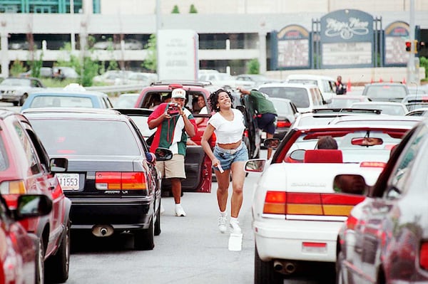 A woman runs back to her car after posing quickly for another Freaknik participant near Phipps Plaza and Lenox Mall. After the malls closed, traffic came to a standstill on Peachtree and Lenox roads during the 1995 gathering. AJC file 1995