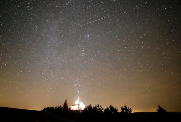 FILE - A meteor streaks across the sky during the annual Geminids meteor shower over an Orthodox church on the local cemetery near the village of Zagorie, Belarus, late, Dec. 13, 2017. (AP Photo/Sergei Grits, File)