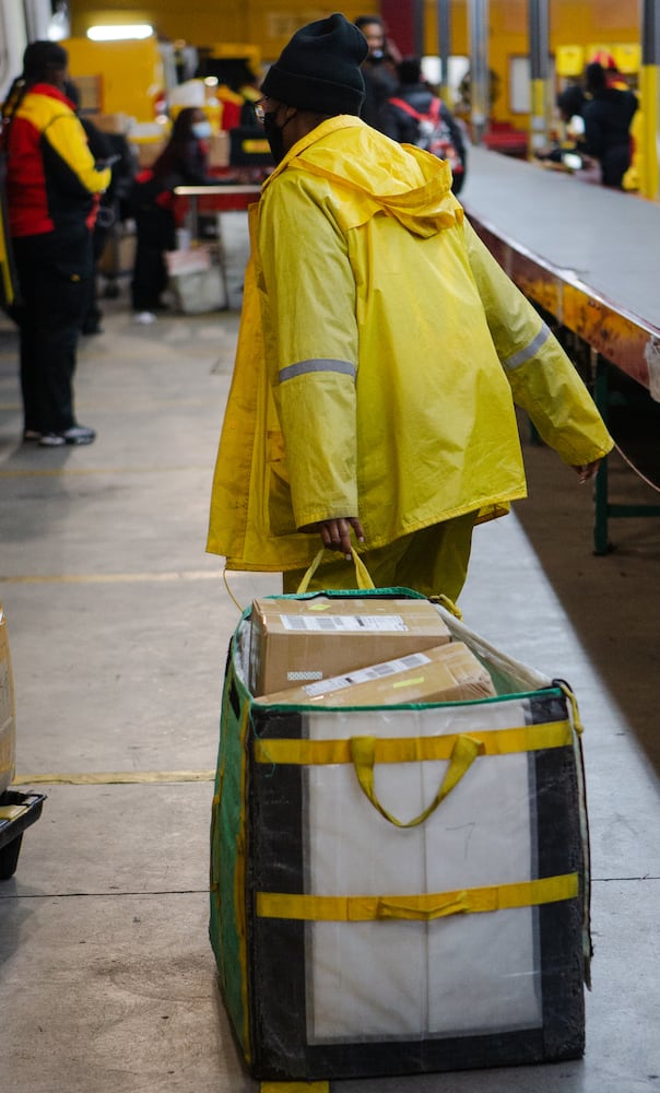 A DHL employee drags a container of boxes across the DHL Express shipping center on Wednesday, December 16, 2020,  in Atlanta. Workers at the shipping center worked to fulfill orders during the holiday rush. CHRISTINA MATACOTTA FOR THE ATLANTA JOURNAL-CONSTITUTION.