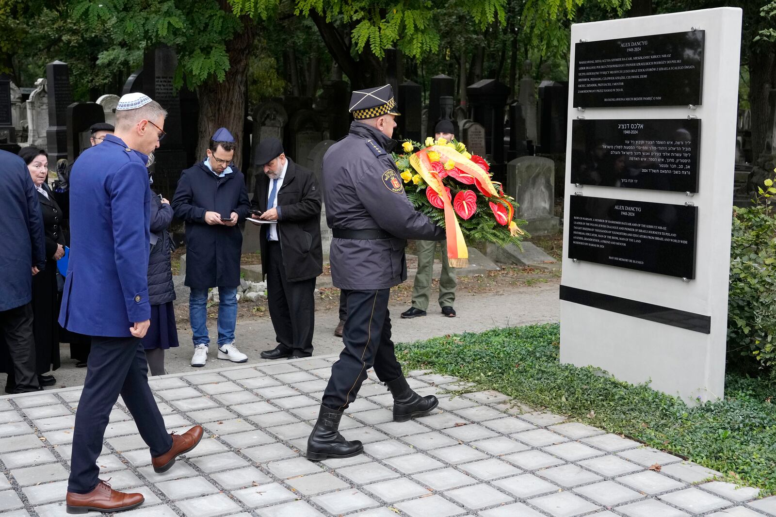 A wreath is brought to a plaque honoring Alex Dancyg, a Polish-Israeli man who was kidnapped by Hamas on Oct. 7, 2023, and later killed, in Warsaw's Jewish cemetery on the one-year anniversary of the Hamas attack, in Warsaw, Poland, on Monday, Oct. 7, 2024. (AP Photo/Czarek Sokolowski)