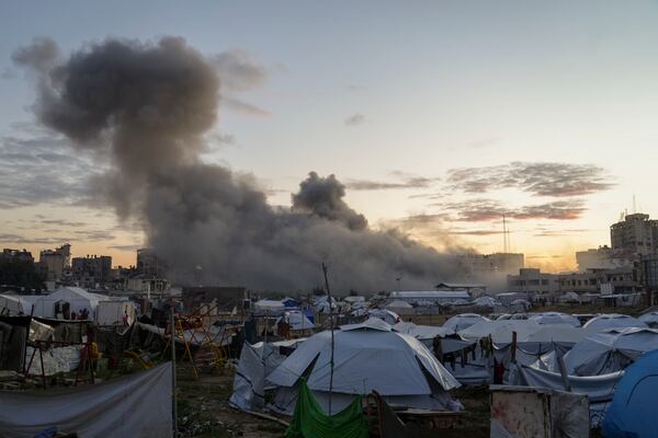 Behind a tent camp for displaced Palestinians, smoke rises from a building after it was targeted by an Israeli army strike, following evacuation orders for residents, in Gaza City, Saturday, March 22, 2025. (AP Photo/Jehad Alshrafi)