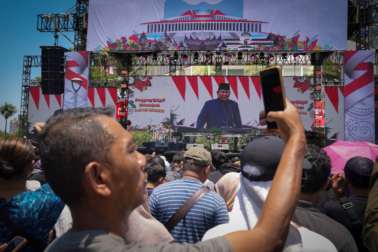 An Indonesia take picture with his cellphone as others watch from a giant screen of Newly-inaugurated Indonesian President Prabowo Subianto speech in Jakarta, Indonesia, Sunday, Oct. 20, 2024. (AP Photo/Dita Alangkara)