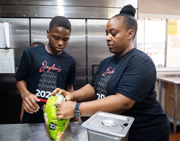 Jaybee’s Tenders co-founder Erika Harrington shows her son Javonte Harrington, 15, how to seal a bag of cheese at Jaybee's Tenders in Decatur, GA on Thursday, July 25, 2024. (Seeger Gray / AJC)