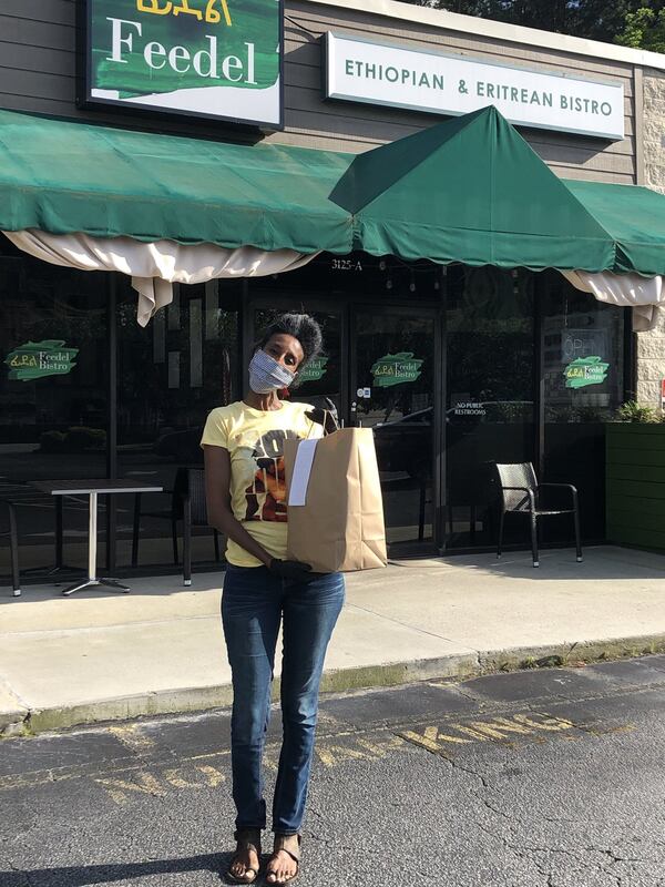 Feedel Bistro co-owner Tamar Telahun brings a takeout order to the parking lot of the Ethiopian and Eritrean restaurant on Briarcliff Road. CONTRIBUTED BY WENDELL BROCK