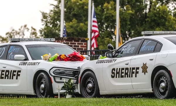 A memorial is growing outside the Cobb County Sheriff's Office, where mourners are leaving flowers on the patrol cars of slain deputies Jonathan Randall Koleski and Marshall Samual Ervin Jr.