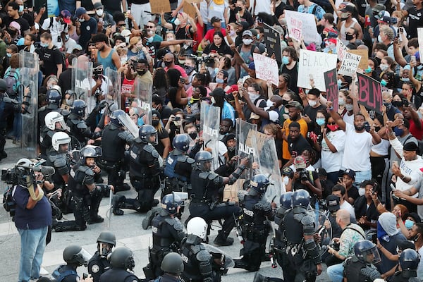 In a show of peace and solidarity, law enforcement officials with riot shields take a knee before protesters during a fourth day of protests on Monday, June 1, 2020, in Atlanta. 