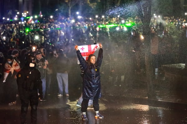 A demonstrator with a Georgian national flag stands under running water from a water cannon rallying outside the parliament's building to continue protests against the government's decision to suspend negotiations on joining the European Union in Tbilisi, Georgia, on Monday, Dec. 2, 2024.(AP Photo/Zurab Tsertsvadze)