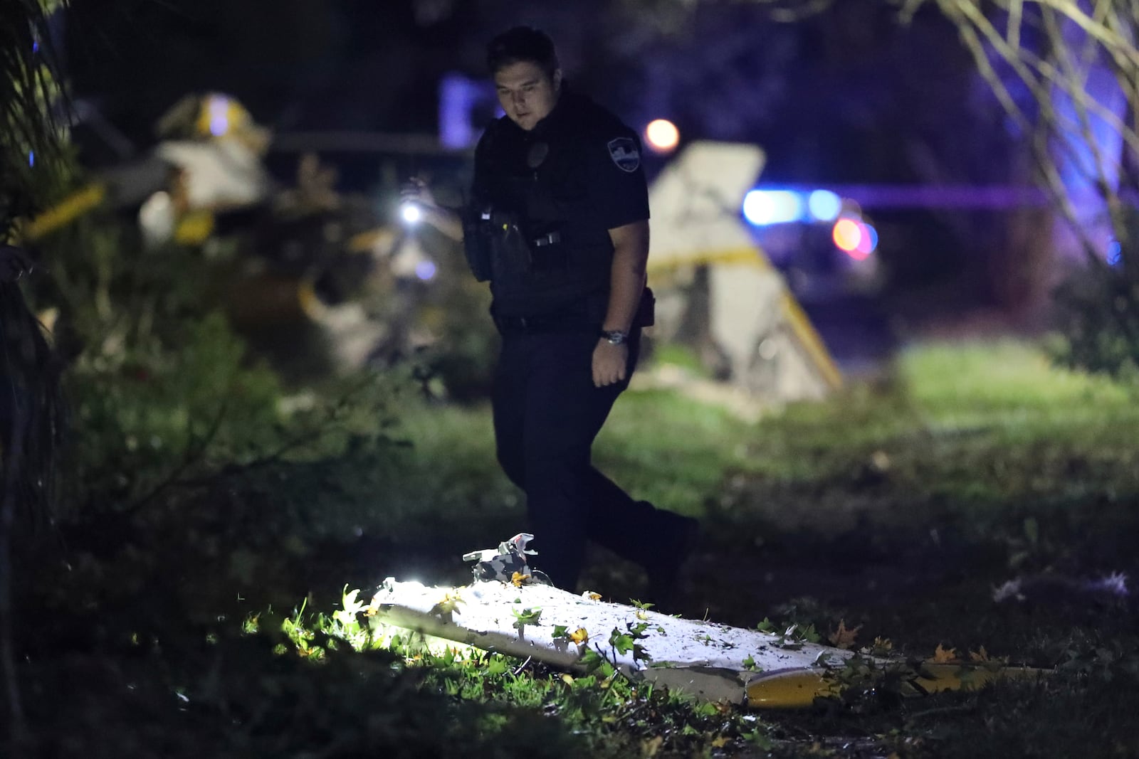 A Savannah Police officer shines his flashlight on a piece of a small Cessna that crashed into the front yard of a home in Savannah, Ga., Sunday, Oct. 13, 2024. (Richard Burkhart/Savannah Morning News via AP)