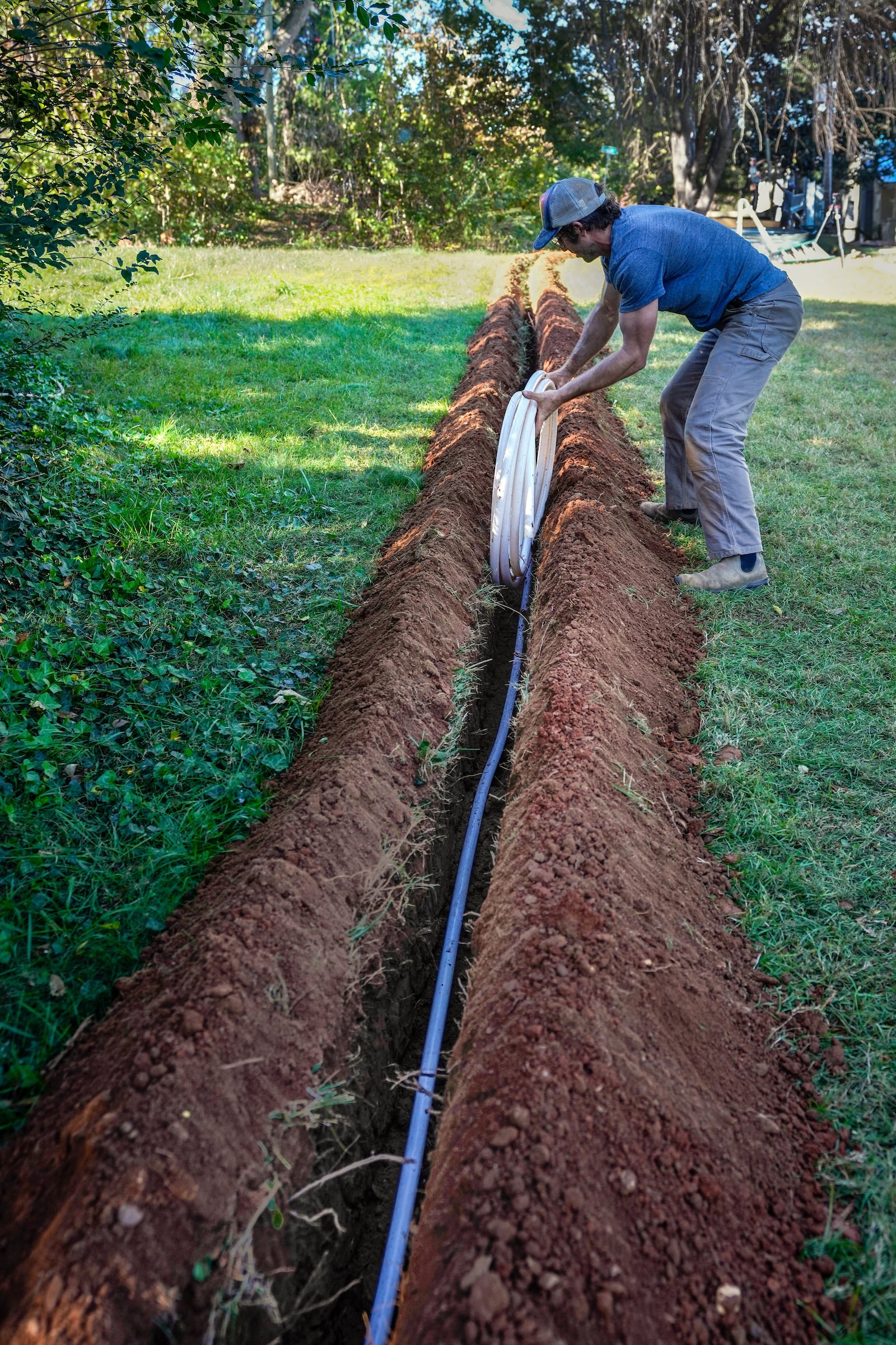 Jeffrey Martyn, a plumber and electrician puts pipe into a freshly made ditch on an urban farm that belongs to Bountiful Cities, a nonprofit organization, Monday, Oct. 14, 2024, in Asheville, N.C. (AP Photo/Kathy Kmonicek)