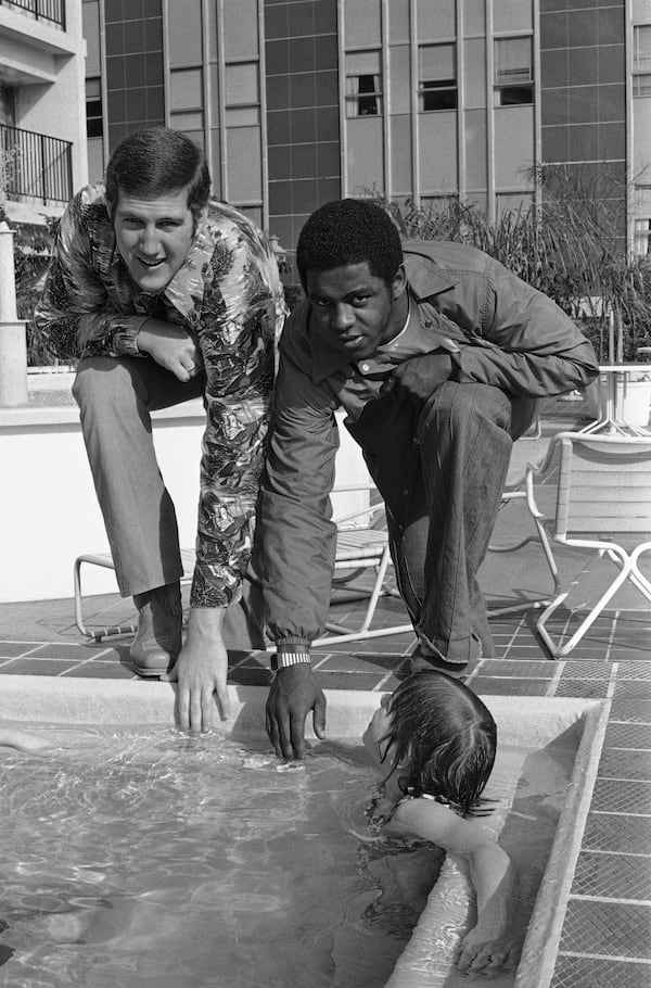 Pittsburgh Heisman Trophy winner Tony Dorsett, right, and Georgia quarterback Ray Goff test the temperature of the pool with a high of 70 degrees expected, Tuesday, Dec. 28, 1976, New Orleans, La. The youngster is 10-year-old Wendy Wait of Richland Center, Wisconsin. They players were together for a press conference during Sugar Bowl activities. (AP Photo)