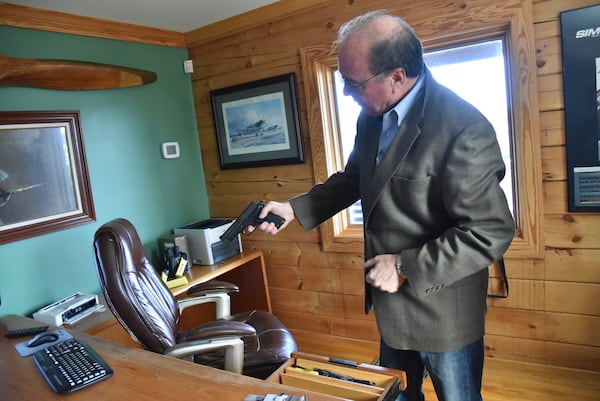 Toland shows off a pistol at his office earlier this month. Toland is a believer in self-reliance — and self-defense. HYOSUB SHIN / HSHIN@AJC.COM