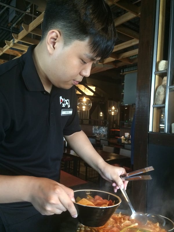 A server at Next Door ladles bowls of budae jjigae (spicy kimchi soup with sausage) to waiting lunchtime diners. CONTRIBUTED BY WENDELL BROCK