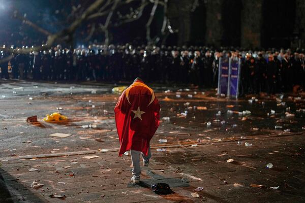 A man with the Turkish flag on his back stands in front of anti riot police officers during clashes in a rally against the arrest of Istanbul's Mayor Ekrem Imamoglu, in Istanbul, Turkey, Friday, March 21, 2025. (AP Photo/Khalil Hamra)