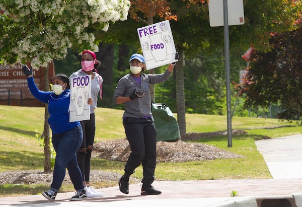 Members of the Pleasant Grove Baptist Church in Marietta hold signs telling motorists about the church's food giveaway Saturday, April 18, 2020.  STEVE SCHAEFER / SPECIAL TO THE AJC