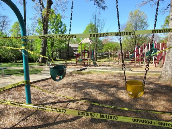 The tennis courts, ball field and dog park are now closed at Lewis Park in Marietta, where a newly posted sign notes new hours and social distancing guidelines. Caution tape blocks use of swings and other playground equipment. Photos: Jennifer Brett, jbrett@ajc.com