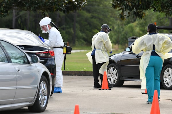 Medical workers in protective gear collect samples at a Phoebe Putney Health System drive-through testing site in Albany on Tuesday. As of Thursday, more than 1,400 people tested through the health system were still awaiting their results. HYOSUB SHIN / HYOSUB.SHIN@AJC.COM