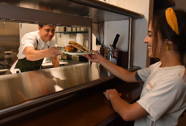 Reid Trapani passes his wife Sophia two vegan Cuban sandwiches from the kitchen of La Semilla. (CHRIS HUNT FOR THE ATLANTA JOURNAL-CONSTITUTION)