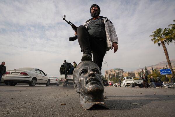 An opposition fighter steps on a broken bust of the late Syrian President Hafez Assad in Damascus, Syria, Sunday Dec. 8, 2024. (AP Photo/Hussein Malla)