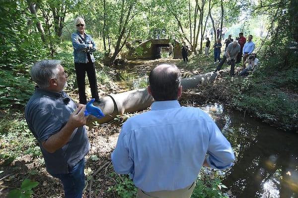 Environmental activist Erin Brockovich (top left) looks on as Bob Bowcock (left) and Ben Finley talk while taking a water sample in a stream near Threadmill Lake in Dalton, Georgia on Sept. 20, 2024. (Courtesy of Matt Hamilton)