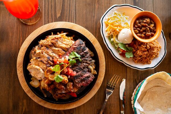 Dos Bocas Deluxe Combo Fajitas, char grilled chicken, steak, shrimp, housemade flour tortillas, onions, peppers, beans, cheese blend, pico de gallo, and sour cream. Photo credit- Mia Yakel.