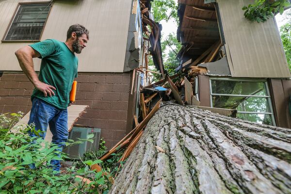 Justin Pfaff of Shackleford Tree Service examines a tree that sliced a home in two on Overbrook Drive. JOHN SPINK / JSPINK@AJC.COM