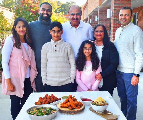 Chef Farhan Momin (second from left in back row) is shown with (back row, from left) sister Arshiya Budwani; father Ahmed Momin; mother Eliza Momin; brother-in-law Nadeem Budwani; (bottom row from left) nephew Ayan Budwani and niece Saira Budwani. On the table in front of them are (from left) Khaman Cornbread, Black-Eyed Pea Vada (Fritters), Tandoori Fried Chicken and Crispy Black-Eyed Pea Chaat. (Styling by chef Farhan Momin / Chris Hunt for the AJC)