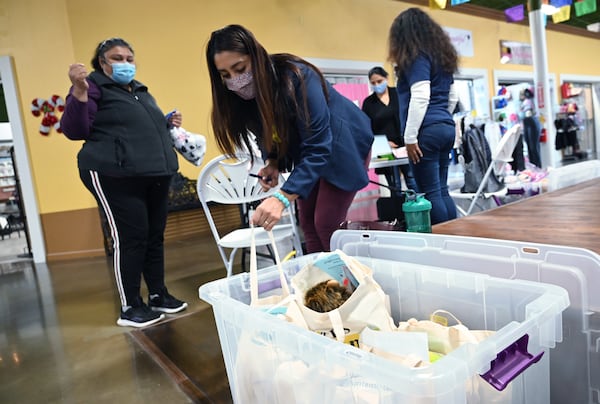 December 9, 2020 Lilburn - Gwinnett County Public Schools' Hispanic Mentoring Program staff Tania Muniz (foreground) hands out a bag of two science experiments and Christmas gift to parent Eloisa Garcia (left) at Plaza Las Americas in Lilburn on Wednesday, December 9, 2020. (Hyosub Shin / Hyosub.Shin@ajc.com)