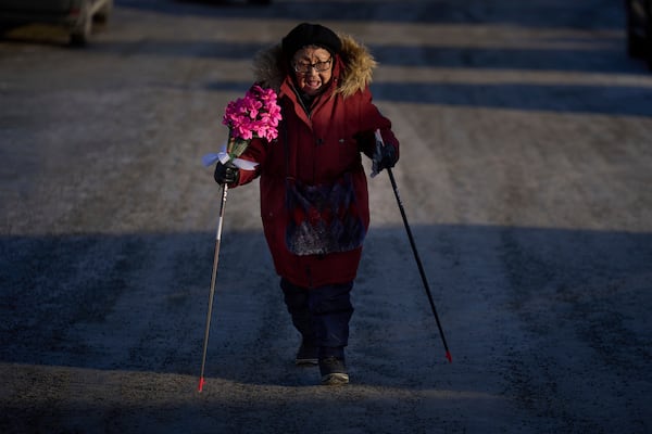 Sussane Isaksen, 79, holds a bunch of flowers as she walks through the snow-covered street to attend her friend's funeral in Nuuk, Greenland, Friday, Feb. 14, 2025. (AP Photo/Emilio Morenatti)