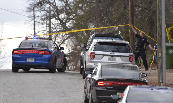 An Atlanta police officer holds up crime-scene tape for a Georgia State Patrol trooper's car in southwest Atlanta. HYOSUB SHIN / HSHIN@AJC.COM