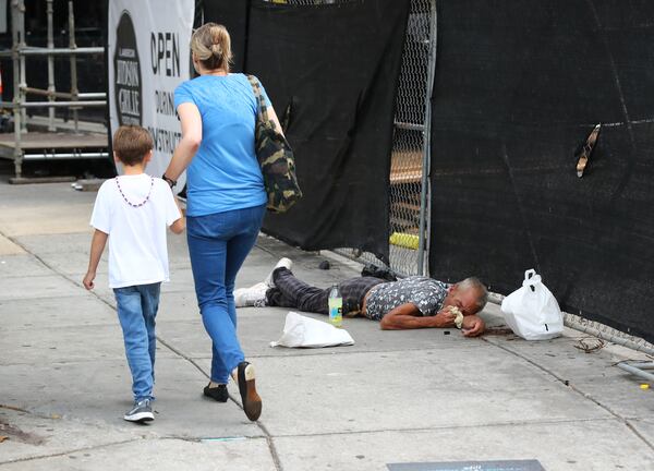 A woman and child pass by a man asleep on the sidewalk along Marietta Street near the CNN Center on Sunday, July 3, 2022, in Atlanta. (Curtis Compton/AJC)