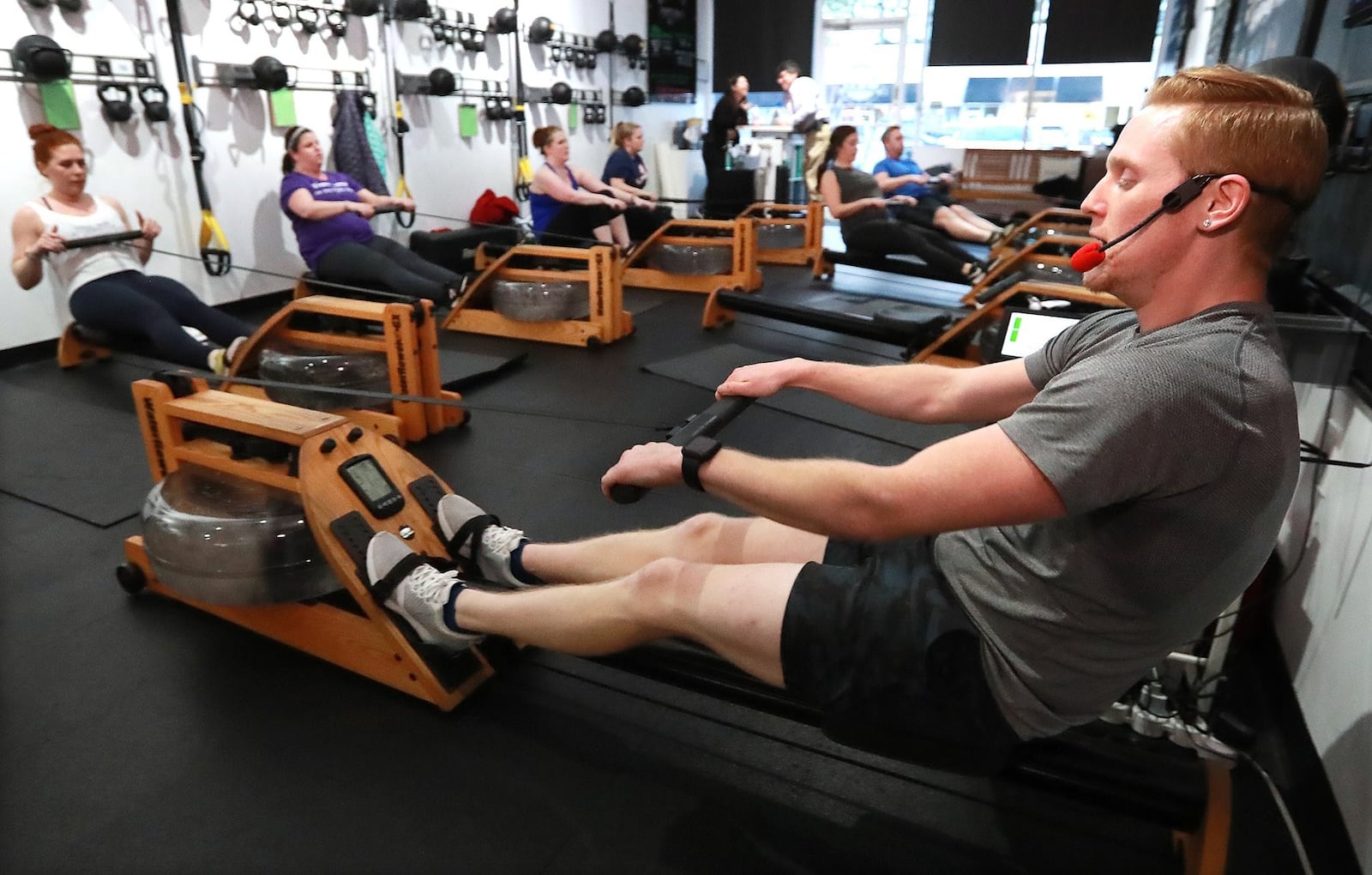 Dylan Loope, a trainer at Total Row Fitness, leads a fitness class on rowing machines in Atlanta. Loope pieces together a living from multiple part-time trainer jobs. Curtis Compton ccompton@ajc.com