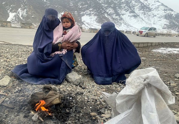 FILE -Gulnaz, left, keep her 18-month-old son warm themselves as they wait for alms in the Kabul - Pul-e-Alam highway eastern Afghanistan, Tuesday, Jan. 18, 2022. (AP Photo/Kathy Gannon, File)