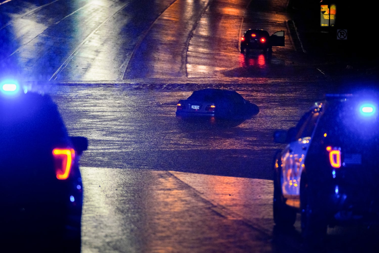 Vehicle sits submerged in flood waters, Marrietta police vehicles block the road. Multiple vehicles were caught in flash flooding early Wednesday morning. Ben Hendren for the AJC