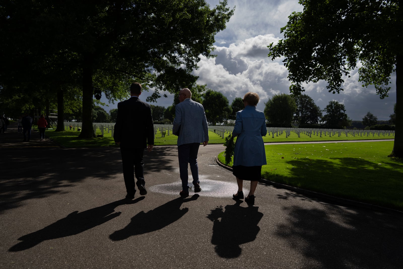 Eighty years after the liberation of the south of the Netherlands, Scott Taylor, left, Ton Hermes, center, and Maria Kleijnen walk to the grave of Scott's grandfather Second Lt. Royce Taylor, a bombardier with the 527 Bomb Squadron, at the Netherlands American Cemetery in Margraten, southern Netherlands, on Wednesday, Sept. 11, 2024. (AP Photo/Peter Dejong)