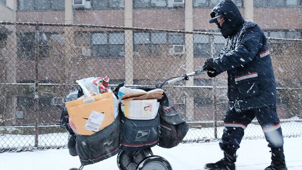 FILE PHOTO: A mail carrier walks through the snow on March 21, 2018 in the Brooklyn borough of New York City. Despite dangers, mail delivery is among the services that continues when weather gets frigid.