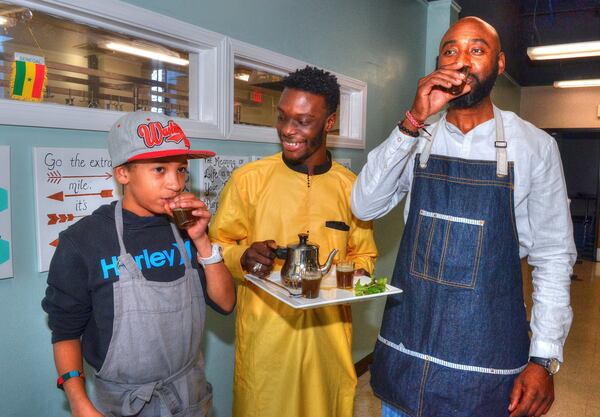 A celebratory cup of Attaya (green tea brewed with fresh mint and sugar) prepared by chef Mouhamed Ndiaye (aka Chef Mo) is enjoyed by Fallou Diouf (from left), Chef Mo and chef Cheikh Ndiaye, just after meal preparation. The two chefs are not related. Their last name is a common one in Senegal. CONTRIBUTED BY CHRIS HUNT PHOTOGRAPHY