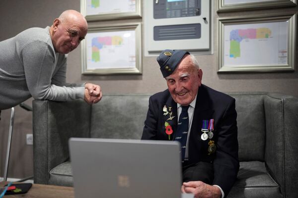 Michael Woods, 100-year-old World War II veteran, right, speaks during a video interview next to his son Eddie in Dunstable, Bedfordshire, England, Tuesday, Nov. 5, 2024. (AP Photo/Kin Cheung)