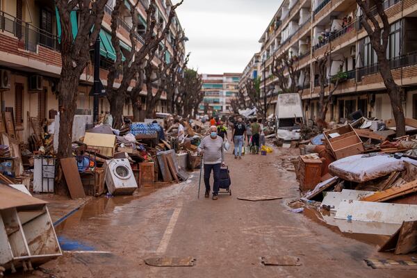 People walk through a street with piled furniture and rubbish on the sides, in an area affected by floods in Benetusser, Spain, on Monday, Nov. 4, 2024. (AP Photo/Manu Fernandez)