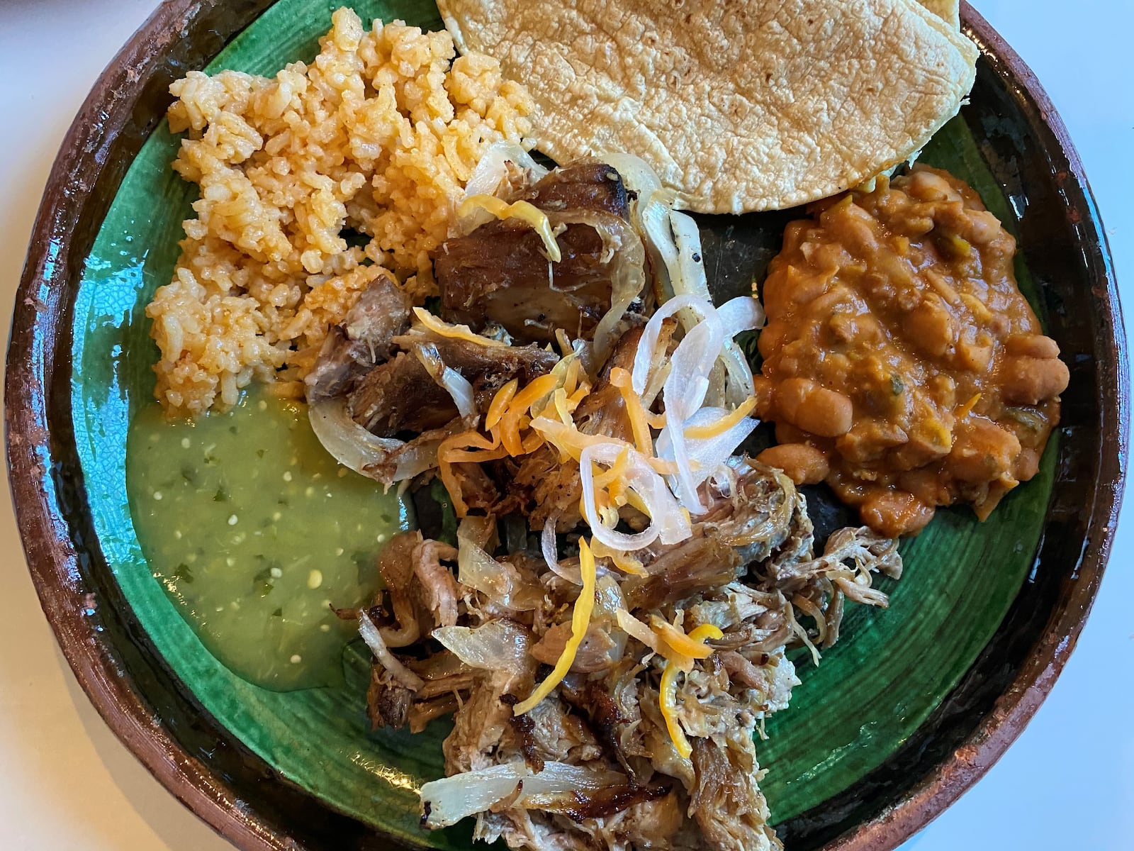 Taqueria el Tesoro's twice-cooked carnitas are seen as plated at home, topped with pickled onions and served with sides of rice and beans and corn tortillas. Bob Townsend for The AJC