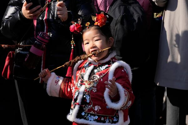 A girl in a traditional dress eats as people gather at the Ditan Temple Fair on the first day of the Chinese Lunar New Year in Beijing on Wednesday, Jan. 29, 2025. (AP Photo/Aaron Favila)