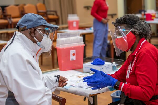 DeKalb County Board of Health medical worker Sandra Armstead, right, explains a few possible symptoms of the COVID-19 vaccination to Army Veteran and Rockdale County resident Larry Mitchell after she administered the vaccine to him last month in Stonecrest. (Alyssa Pointer / Alyssa.Pointer@ajc.com)