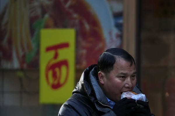 A man eats a pancake as he walks by a noodles restaurant during a morning rush hour in Beijing, Thursday, March 6, 2025. (AP Photo/Andy Wong)