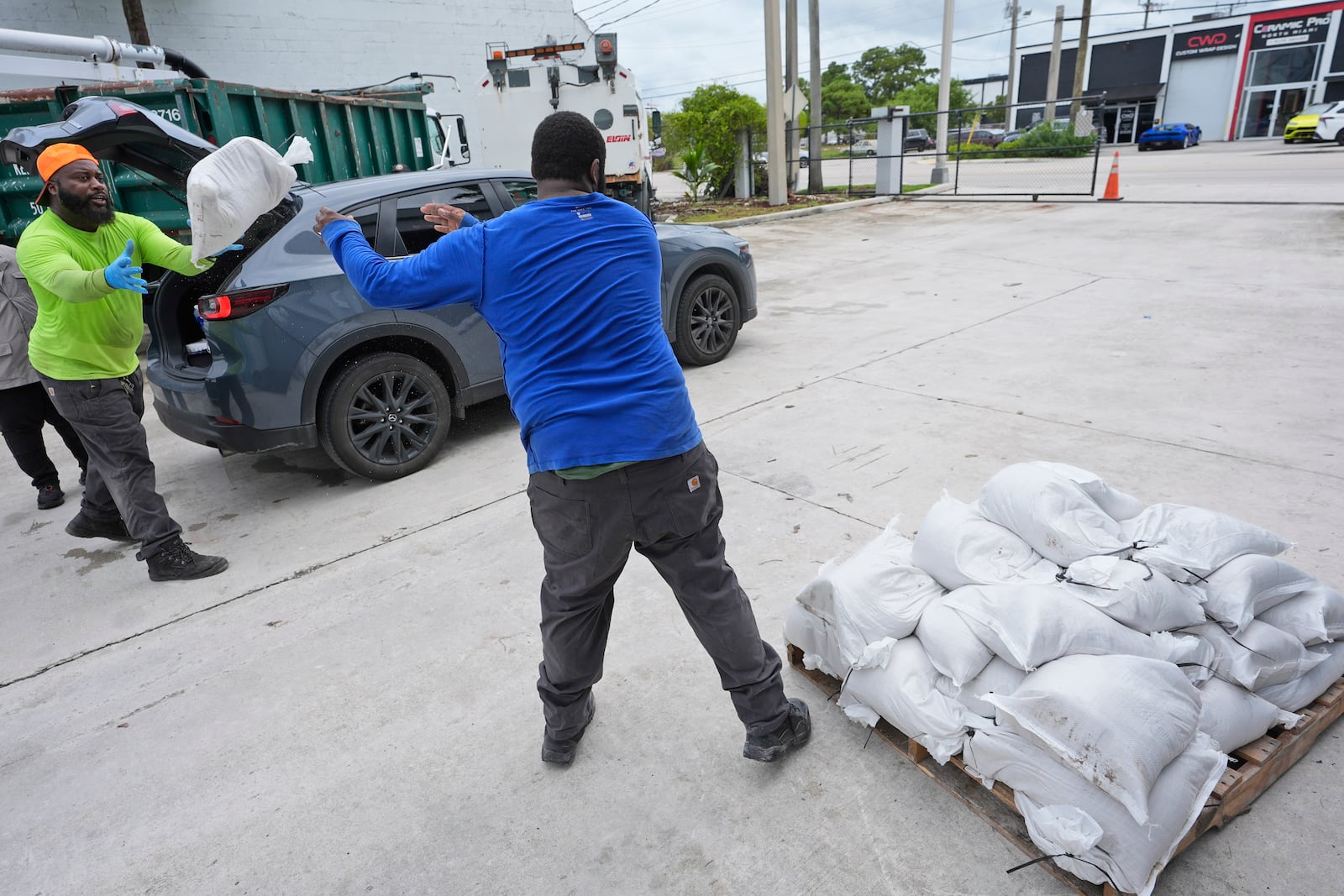 North Miami Beach, Fla., public service workers Roshad Smiley, left, and Mikhail Pollar, foreground, load sandbags to help prevent flooding, to residents cars as Hurricane Milton prepares to strike Florida, Tuesday, Oct. 8, 2024, in North Miami Beach. (AP Photo/Wilfredo Lee)