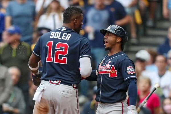 Braves right fielder Jorge Soler (12) is congratulated by second baseman Ozzie Albies (1) after Soler beat the tag by Milwaukee Brewers catcher Manny Pina (9) to score on a RBI single by Freddie Freeman (5) in the third inning of Game 2 of the NLDS Saturday, Oct. 9, 2021, in Milwaukee. (Curtis Compton / Curtis.Compton@ajc.com)