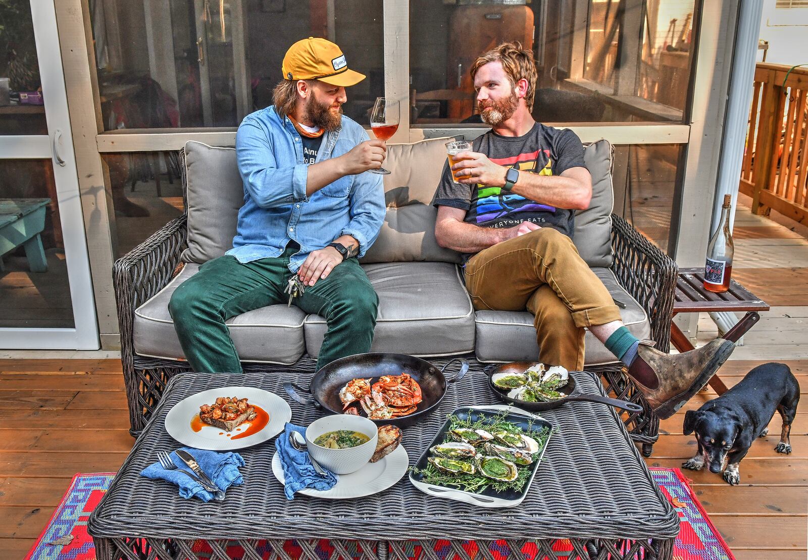 Kimball House executive chef Brian Wolfe (left) and Bryan Rackley, the restaurant's resident oyster expert and purveyor, toast each other's talents and efforts during a very difficult time for restaurants. On the table in front of them at Rackley's home are (from left) Shellfish Escabeche (on bread), Oyster Stew, Shellfish Escabeche served in blue crab (center top), Roasted Oysters (upper right in pan) and Grilled Oysters (lower right in tray). (Food styling by Brian Wolfe and Bryan Rackley/Chris Hunt fFor The AJC)