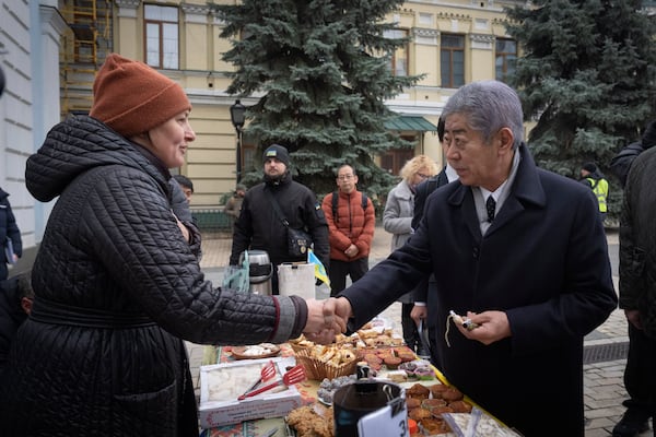 Japanese Foreign Minister Takeshi Iwaya shakes hands with a seller at a charity volunteer sale to donate the Ukrainian army in Kyiv, Ukraine, Saturday, Nov. 16, 2024. (AP Photo/Efrem Lukatsky)