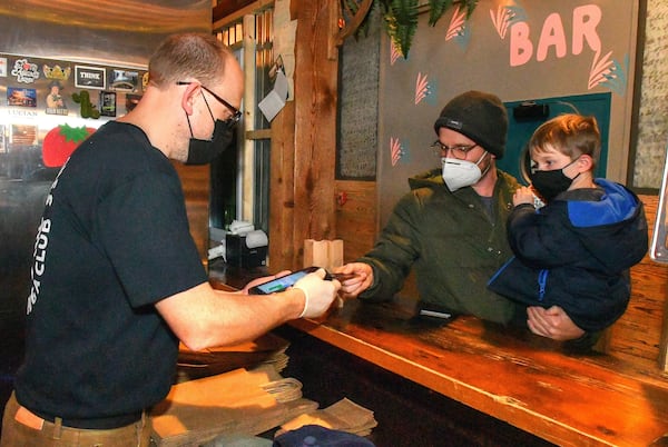 211220 Atlanta, Ga: Ticonderoga Club co-owner Greg Best (left) makes a transaction with longtime customer Gardner Rordam and son Graham (6), both of Atlanta, at the walk-up window at the Club at Krog Street Market Monday 12/20/21 afternoon. (Chris Hunt for The Atlanta Journal-Constitution)